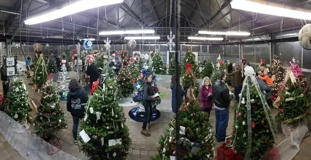 Visitors browsing rows of decorated Christmas trees at the Rochester Festival of Trees at Studley's Flower Gardens