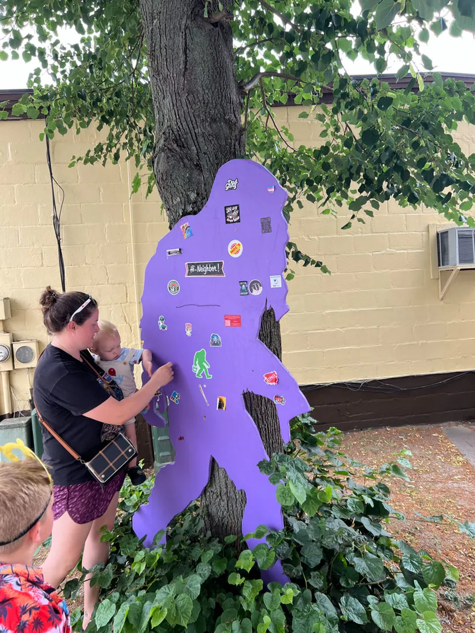 A family finding a purple Bigfoot cutout hidden beside a tree in downtown Rochester