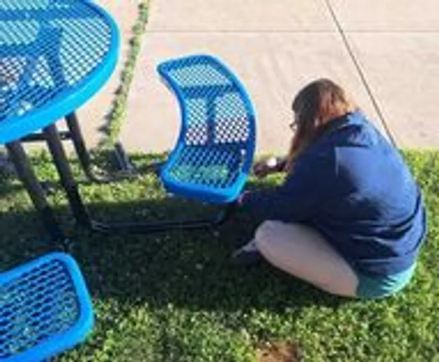 A volunteer assembling a bright blue bistro table and chairs downtown